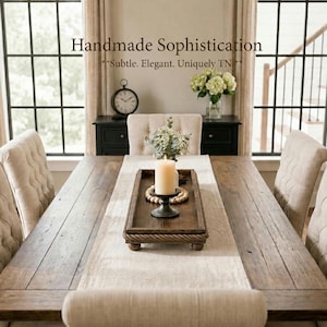 May include: A rectangular dark brown wooden tray with a rope border and small feet, holding a cream pillar candle on a black stand and a small vase of white flowers. The text "Handmade Sophistication **Subtle. Elegant. Uniquely TN**" is visible.
