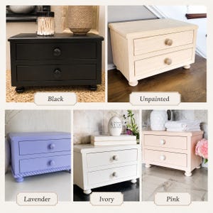 May include: A collection of five wooden desktop organizers, each featuring two drawers with round knobs and four bun feet. The organizers are shown in five distinct finishes: matte black, natural unpainted wood, lavender, ivory, and soft pink.