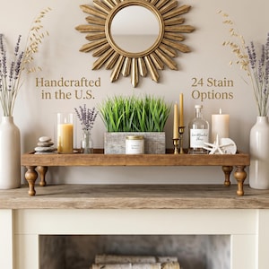May include: A wooden decorative tray with turned legs, holding candles, a small plant, and a bottle. The tray is on a wooden surface, with a sunburst mirror above. Text reads "Handcrafted in the U.S." and "24 Stain Options".