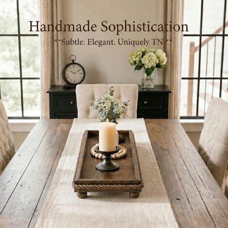 May include: A rectangular dark brown wooden tray with rope detailing and four small feet, holding a cream-colored pillar candle in a black metal holder and a string of wooden beads. Text reads: Handmade Sophistication **Subtle. Elegant. Uniquely TN **