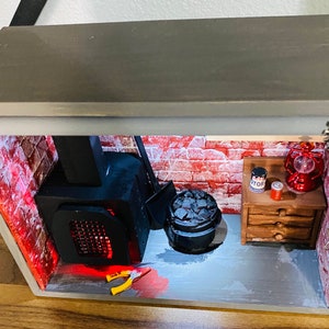 May include: A miniature diorama of a brick basement with a black wood-burning stove, a black metal bucket with coal, a small wooden dresser with a red can labeled "Motor", a red lantern, and a metal gear.