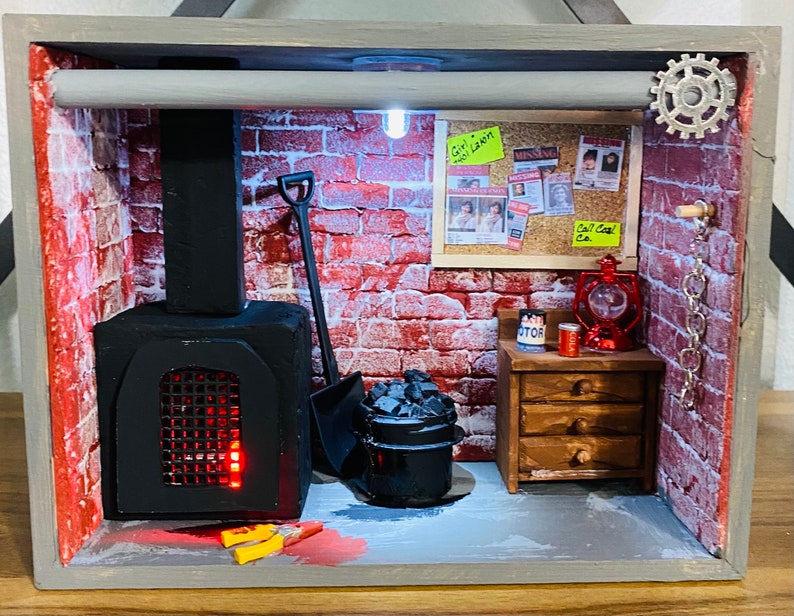 May include: A miniature diorama of a brick building with a black fireplace, a small wooden dresser, and a red lantern. The diorama is decorated with a brick wall, a metal pipe, and a sign that reads "Girl Lost".