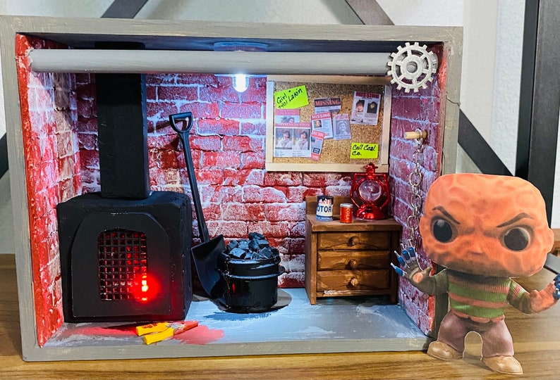 May include: A miniature diorama of a basement with a brick wall, a black metal furnace, a shovel, a bucket of coal, a wooden dresser, a red lantern, and a Freddy Krueger Funko Pop figure.