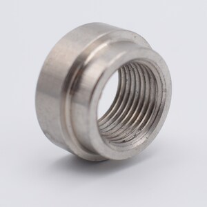 May include: A close-up of a stainless steel threaded fitting. The fitting is cylindrical with a wider outer ring and a threaded inner diameter. The metal has a brushed finish and reflects the surrounding light.