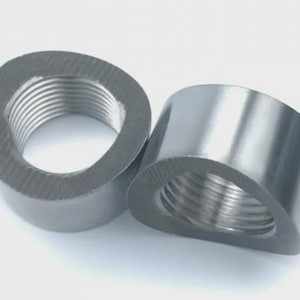 Può includere: Due raccordi per tubi grigio metallizzato, angolati, con filettatura interna. I raccordi sono cilindrici con un lato piatto e angolato, su sfondo bianco. La filettatura è visibile all'interno delle aperture.