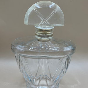 May include: A clear glass perfume bottle with a faceted design and a clear plastic stopper with a geometric pattern.