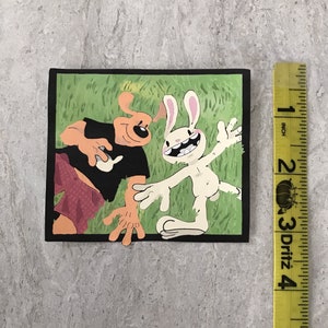 Op de afbeelding: Een zwart-witte cartoonillustratie van een hond en een konijn. De hond draagt een zwart shirt en een rode broek. Het konijn draagt niets. De illustratie is tegen een groene achtergrond.