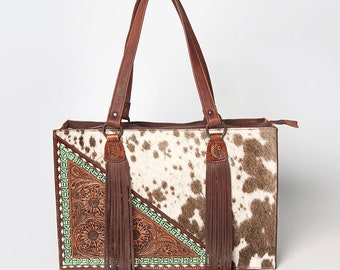 May include: A brown leather tote bag with a white and brown cowhide pattern. The bag has two brown leather straps and two brown leather tassels. The bag is decorated with a green and brown floral design.