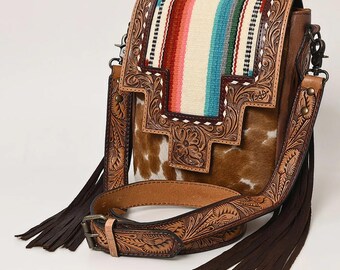 May include: A brown leather crossbody bag with a colorful striped fabric panel and intricate floral tooled detailing. The bag has a long strap with a buckle and fringe accents.