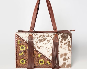 May include: A brown leather tote bag with a white and brown cowhide pattern. The bag has a zipper closure and two long brown leather straps with fringe. The bag is decorated with yellow sunflowers.