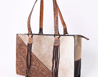 May include: A brown leather tote bag with fringe details and a white and brown cowhide design. The bag has a zipper closure and two top handles.