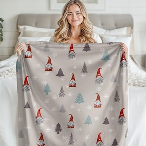 May include: A beige throw blanket with a repeating pattern of gnomes wearing red hats, snowflakes, and stylized pine trees.