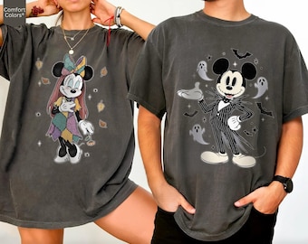 May include: Two dark gray t-shirts featuring Disney characters. One shirt has a Minnie Mouse design in a patchwork dress, and the other has a Mickey Mouse design in a pinstripe suit with bats and ghosts. The shirts are part of a Halloween-themed collection.