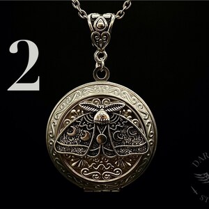 May include: Silver locket necklace with a detailed design of a moth with crescent moons on its wings. The locket is open and has a small chain attached to the top.