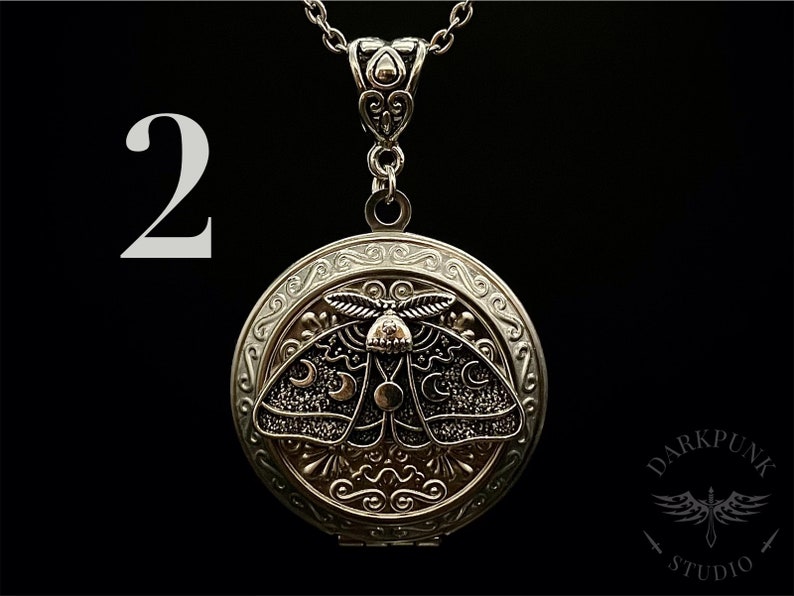 May include: Silver locket necklace with a detailed design of a moth with crescent moons on its wings. The locket is open and has a small chain attached to the top.