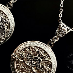 May include: Two silver locket necklaces with intricate designs featuring a moth and a crescent moon. The lockets are open to reveal a detailed design of a moth with wings spread.