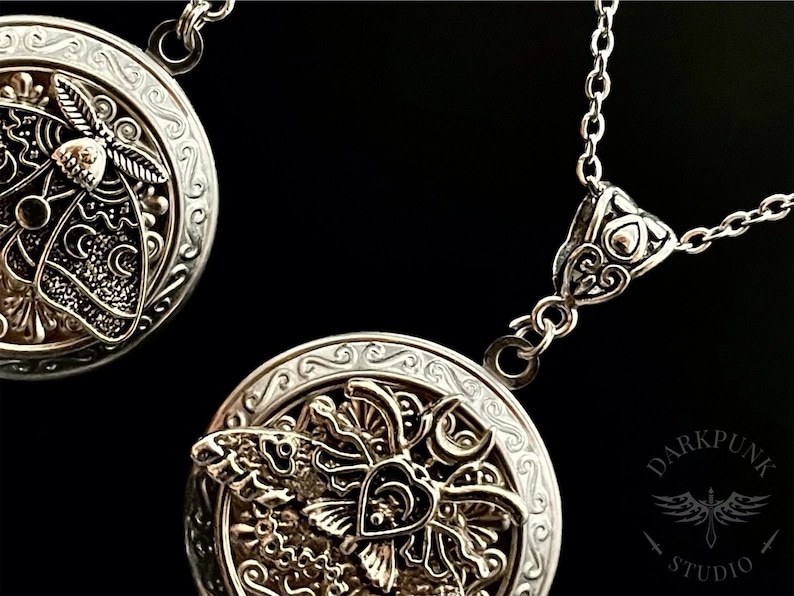 May include: Two silver locket necklaces with intricate designs featuring a moth and a crescent moon. The lockets are open to reveal a detailed design of a moth with wings spread.