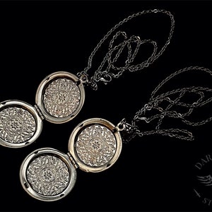 May include: Two silver locket necklaces with intricate floral designs on the front. The lockets are open and the chains are intertwined.