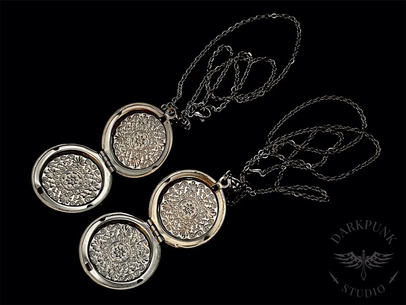 May include: Two silver locket necklaces with intricate floral designs on the front. The lockets are open and the chains are intertwined.