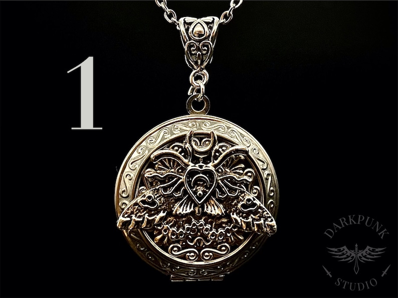 May include: Silver locket necklace with a detailed design of a moth with wings spread. The moth has a heart-shaped body with a skull and crossbones design.