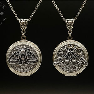 May include: Two silver locket necklaces with a detailed design featuring a moth with moon and star accents. The lockets are open to reveal a blank interior.