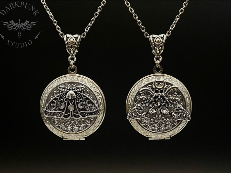 May include: Two silver locket necklaces with a detailed design featuring a moth with moon and star accents. The lockets are open to reveal a blank interior.