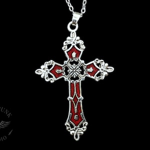 May include: A silver pendant necklace featuring a red enamel cross. The cross has a detailed design with intricate flourishes.