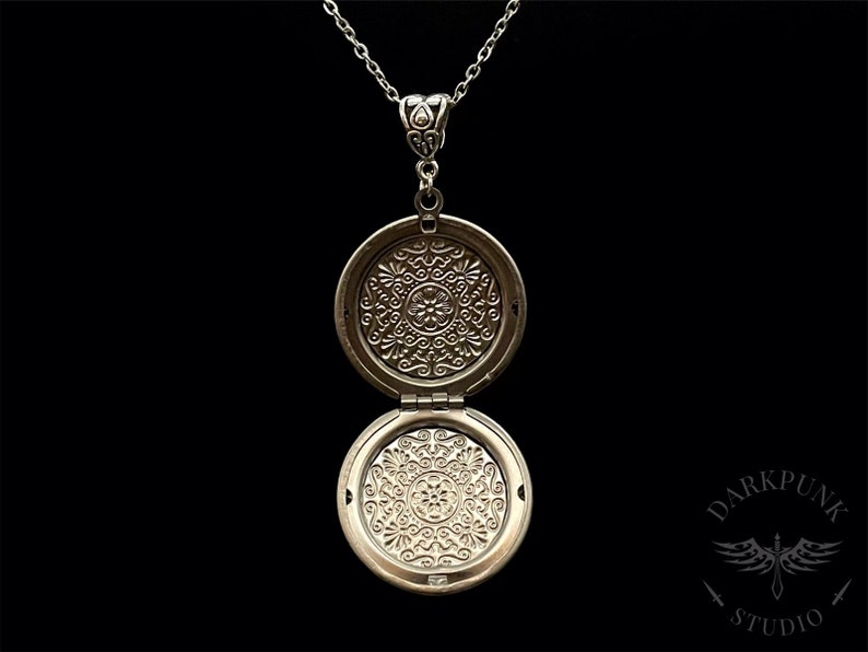 May include: Silver locket necklace with an intricate floral design on the front and back. The locket is open, revealing the inside.