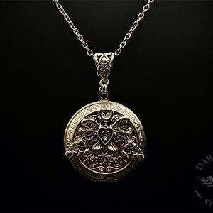 May include: A silver locket necklace with a detailed design of a moth with open wings. The locket is round and has a delicate chain.