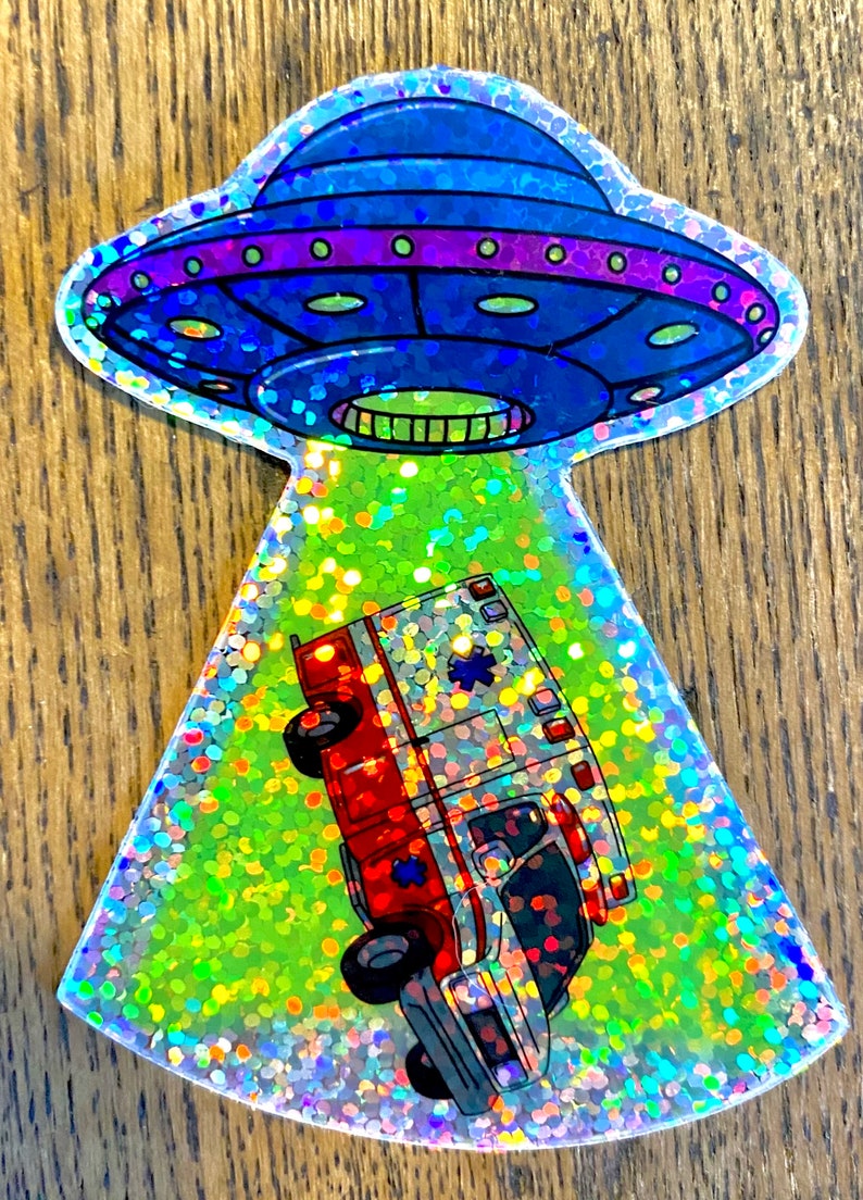 以下が含まれることがあります： 青と紫のUFOが赤と白の救急車を照らしているホログラフィックステッカーです。