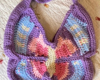 May include: A crocheted butterfly-shaped bag with a purple strap and pink, blue, and white accents.