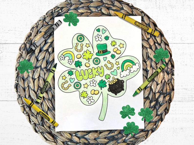 Pu&ograve; includere: Una pagina da colorare in bianco e nero di un trifoglio a quattro foglie con la parola "LUCKY" al centro. Il trifoglio &egrave; circondato da varie immagini a tema San Patrizio, tra cui arcobaleni, monete d'oro, ferri di cavallo e trifogli. La pagina &egrave; circondata da trifogli di glitter verde e matite gialle.