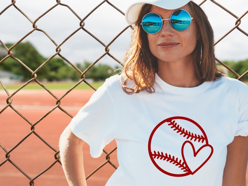 May include: A white t-shirt with a red baseball and heart design. The baseball has white stitching and the heart is inside the baseball.