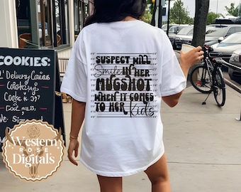 May include: White t-shirt with a black graphic print of a mugshot with the text "SUSPECT WILL Smile IN HER MUGSHOT WHEN IT COMES TO HER Kids".