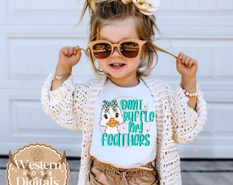 May include: A young child wearing sunglasses, a white t-shirt with a duck graphic and the text "Don't Ruffle My Feathers", a cream-coloured cardigan, and khaki shorts. The child is smiling and holding their hair.