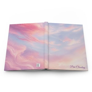 May include: An open hardcover book featuring a continuous wraparound print of a sunset sky with soft pink, purple, and blue clouds. The back cover displays a small square QR code and the text Pink Clouding in a dark purple cursive script font.
