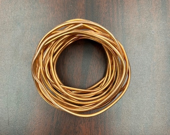 May include: A coil of copper wire, wound into a tight circle, on a brown wooden surface.