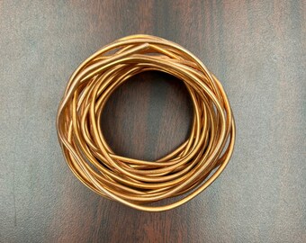 May include: A coil of copper wire, wound into a tight circle, on a brown wooden surface.