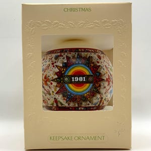 May include: A white Christmas ornament with a colorful starburst design and the year 1981 in the center. The ornament is in a white box with the words "Christmas" and "Keepsake Ornament" printed on it.