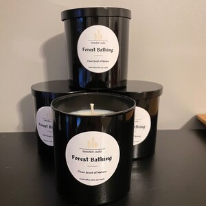 May include: Three black candle jars with white labels. The labels read "bewitched crafts Forest Bathing Clean Scent of Nature Handmade soy wax candle".