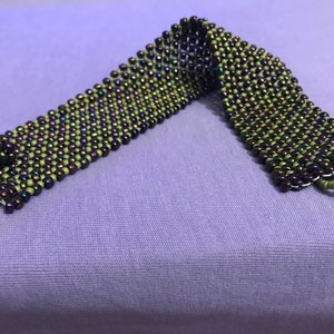 May include: A green and purple beaded bracelet with a woven design.