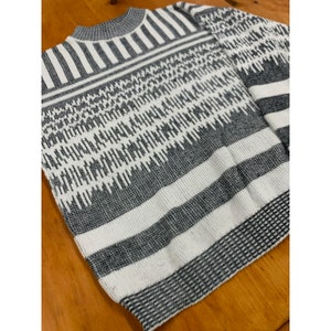 Peut inclure: Un pull à col ras du cou à motifs gris et blancs. Le pull présente un motif géométrique avec des rayures horizontales et un motif texturé. Les manches sont longues et l'ourlet inférieur est côtelé. Le pull est en matière tricotée douce.