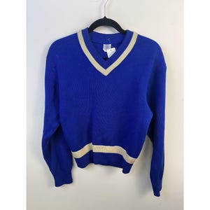 May include: A blue knitted sweater with a white v-neck and white stripe at the bottom.