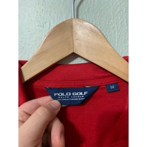 May include: Red polo shirt with a blue Polo Golf Ralph Lauren tag. The tag says "100% Pima Cotton Made in Peru" and has a size M label.