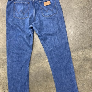 May include: A pair of blue denim jeans with a brown leather patch on the back pocket that says "Wrangler".