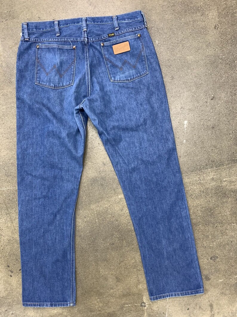 May include: A pair of blue denim jeans with a brown leather patch on the back pocket that says "Wrangler".