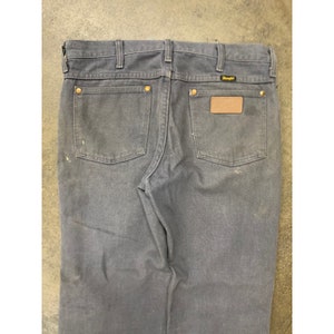 May include: A pair of dark blue denim jeans with a brown leather patch on the back pocket that says "Wrangler".