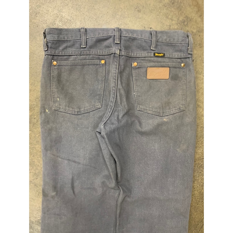 May include: A pair of dark blue denim jeans with a brown leather patch on the back pocket that says "Wrangler".