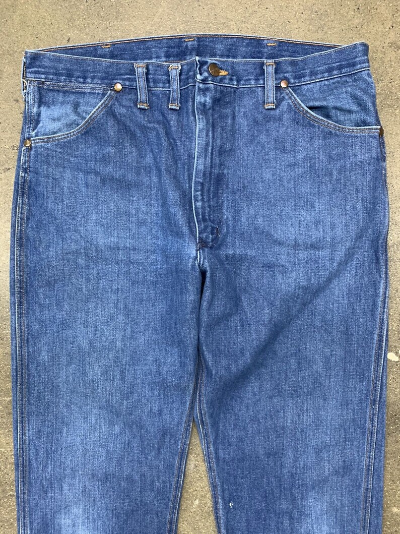 May include: A pair of blue denim jeans with a straight leg fit. The jeans have a classic five-pocket design and a button fly.