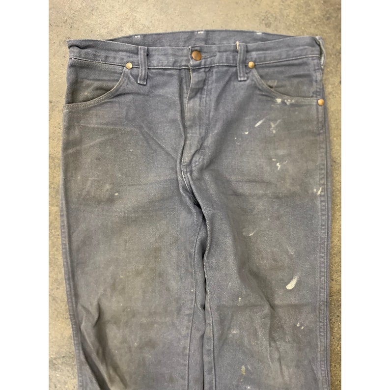 May include: A pair of dark gray denim jeans with white paint splatters. The jeans have a classic five-pocket style and a straight leg.